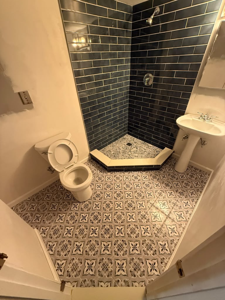 Corner shower with dark subway tile and patterned floor tile